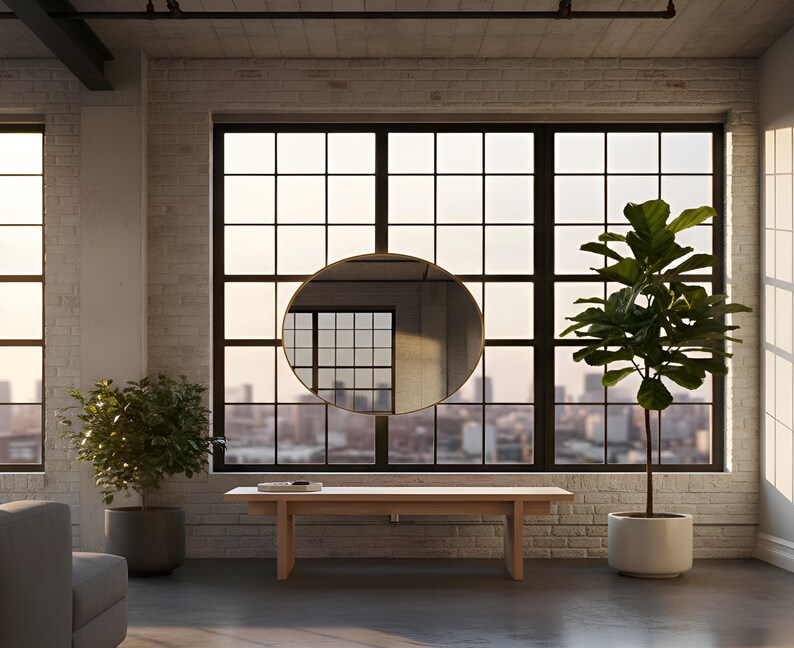 May include: A modern interior with a large window overlooking a cityscape. A round, gold-framed mirror hangs in front of the window. A light wood bench and potted plants are in the room. The walls are white brick.