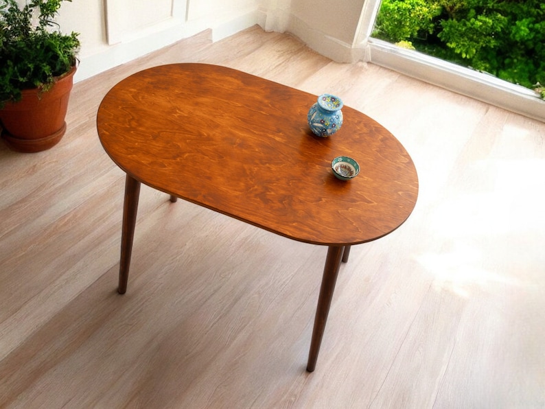 May include: Oval wooden coffee table with a rich brown finish and four slender, dark brown legs. The table has a smooth surface and is adorned with two small decorative ceramic pieces. The table is approximately 122 cm long.