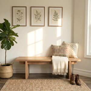 May include: A light wood bench with a cream-colored throw blanket, decorative pillows, and brown leather boots. Three framed botanical prints hang above the bench. A large potted plant and a woven rug complete the cozy interior scene.