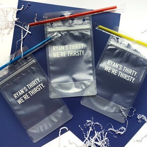 Puede incluir: Tres bolsas de pl&aacute;stico transparentes con cierre de cremallera. Cada bolsa tiene el texto "Ryan's Thirty. We're Thirsty." impreso en blanco.