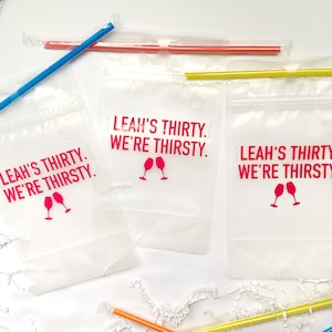 Puede incluir: Tres bolsas de pl&aacute;stico transparentes con cierre de cremallera y un agujero en la parte superior. Cada bolsa tiene un dise&ntilde;o rosa que dice "Leah's Thirty. We're Thirsty." con un gr&aacute;fico de dos copas de vino.
