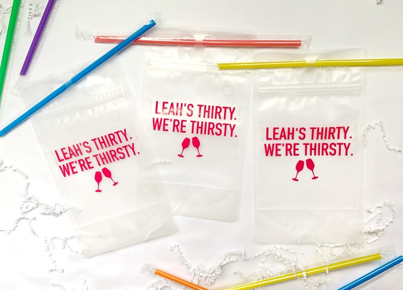 Puede incluir: Tres bolsas de pl&aacute;stico transparentes con cierre de cremallera y un agujero en la parte superior. Cada bolsa tiene un dise&ntilde;o rosa que dice "Leah's Thirty. We're Thirsty." con un gr&aacute;fico de dos copas de vino.