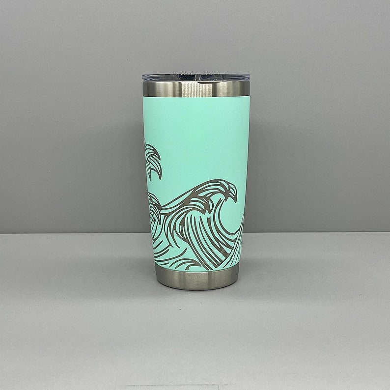 K&ouml;nnte beinhalten: Ein Edelstahlbecher mit einer hellblauen Pulverbeschichtung und einem Design aus Wellen und Palmen.