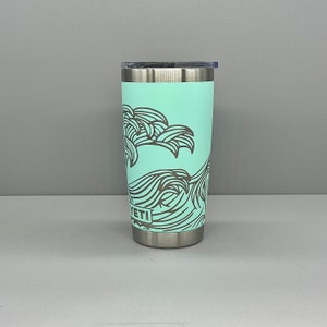 K&ouml;nnte beinhalten: Ein Edelstahlbecher mit hellblauer Au&szlig;enseite und einem schwarz-wei&szlig;en Wellendesign. Der Becher hat einen Deckel und das Wort "YETI" ist auf der Seite aufgedruckt.