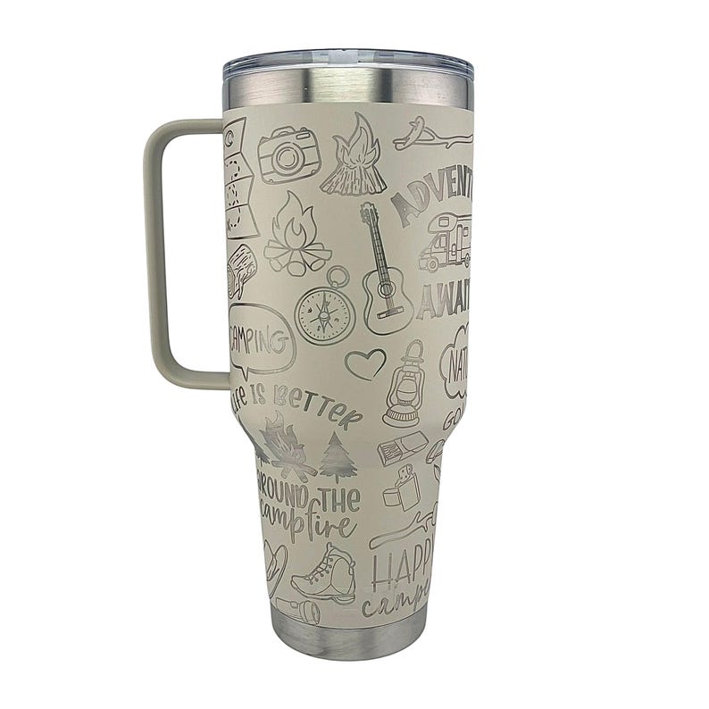 K&ouml;nnte beinhalten: Eine Edelstahl-Reisebecher mit Henkel. Der Becher ist wei&szlig; mit einem grauen Design aus Camping-Motiven und Texten, darunter "Adventure Awaits", "Nature is Better" und "Around the Campfire".