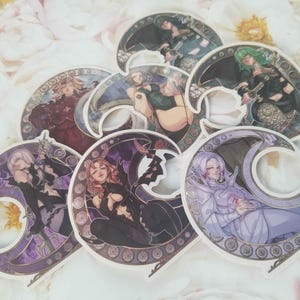 May include: Six colourful stickers featuring different characters in a crescent moon design. Each sticker has a detailed background with a gold and purple border.