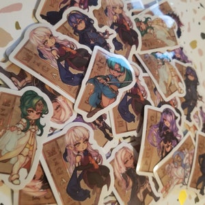 May include: A collection of colourful anime-style character stickers featuring various characters with different hairstyles and clothing. The stickers are printed on white paper with a brown border and text that reads "MICAIAH" and "LYNN".