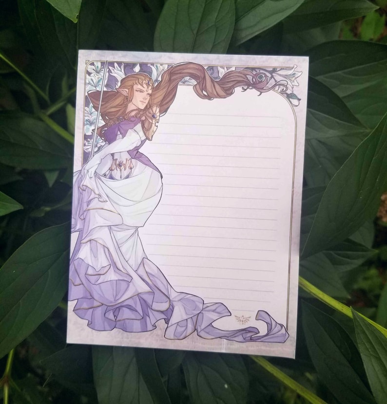 May include: A purple and white illustrated stationery set featuring a female character with long brown hair and a purple dress. The character is holding a sword and has a crown on her head. The stationery set has a lined writing area and a decorative border.