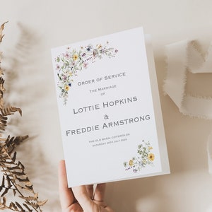 May include: A white wedding ceremony order of service with a floral design. The text reads "Order of Service, The Marriage of Lottie Hopkins & Freddie Armstrong, The Old Barn, Cotswolds, Saturday 29th July 2023."