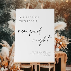 May include: White sign with black text that reads "All because two people swiped right."  The sign also includes the names Arthur & Ophelia, the location "The Old Hay Barn, Cotswolds", and the date "28.08.2027".