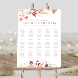May include: A wedding seating chart with an autumn theme. The chart features a watercolour illustration of autumn leaves in shades of orange, red, and yellow. The text reads "Please take your seats Arthur & Ophelia The Old Hay Barn, Cotswolds, Saturday 25th September 2021".