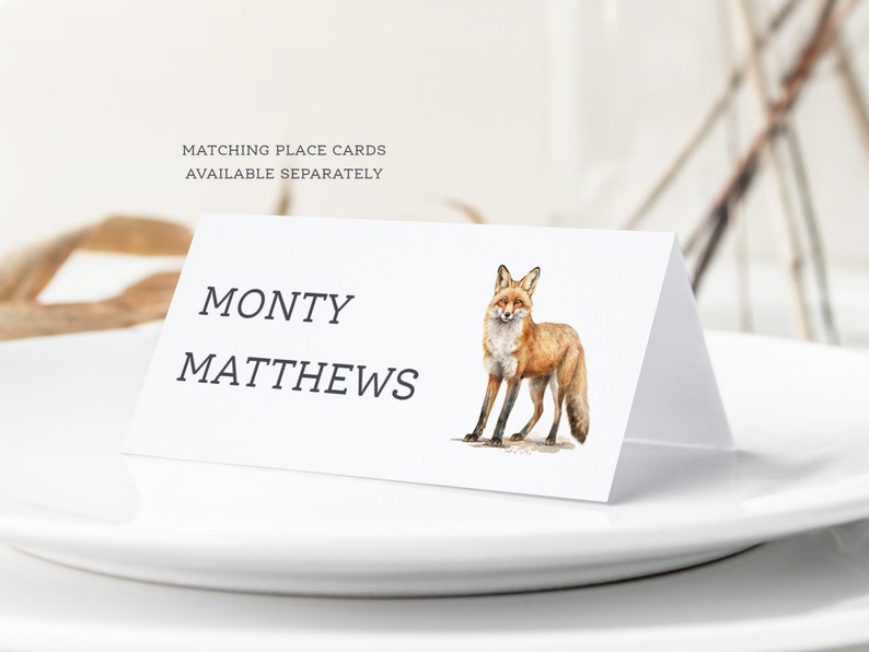 May include: A white place card with the name "MONTY MATTHEWS" printed in black text. A watercolor illustration of a red fox is on the right side of the card.