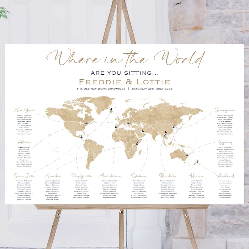 May include: A seating chart for a wedding reception with a world map background. The map is beige with brown lines and black pins. The text "Where in the World" is written in a cursive font at the top of the chart. The text "Are you sitting... Freddie & Lottie" is written below the map. The text "The Old Hay Barn, Cotswolds | Saturday 26th July 2025" is written below the names.