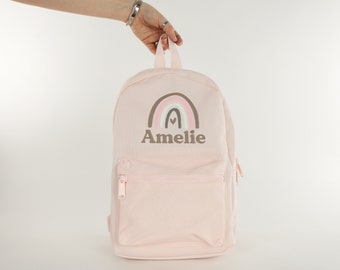 May include: A pink backpack with a rainbow and the name "Amelie" embroidered on the front.