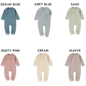 May include: A collection of six baby footed pajamas in various colors: ocean blue, grey blue, sage, dusty pink, cream, and mauve. Each one-piece garment has long sleeves and a button-up front. The names of the colors are displayed above each pajama.