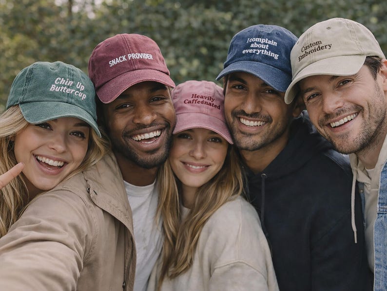 May include: A group of smiling people wearing various colored baseball caps. The caps are in shades of green, burgundy, pink, navy blue, and tan. Each cap has white embroidered text, including phrases like "Chin Up Buttercup" and "Custom Embroidery."