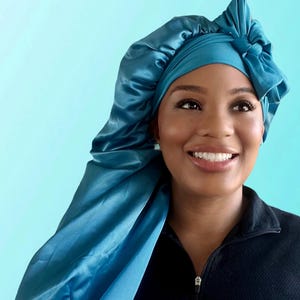 May include: A teal blue satin sleep cap with a bow on top. The cap is designed to protect hair while sleeping.