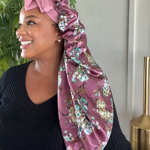 May include: A pink satin sleep cap with a floral print. The cap has a bow on top and is designed to protect hair while sleeping.