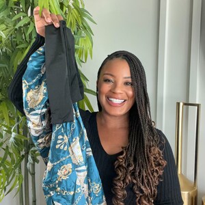 May include: A woman with long braids is holding up a teal blue and gold satin bag with a black fabric handle. The bag has a pattern of chains and ornate designs.