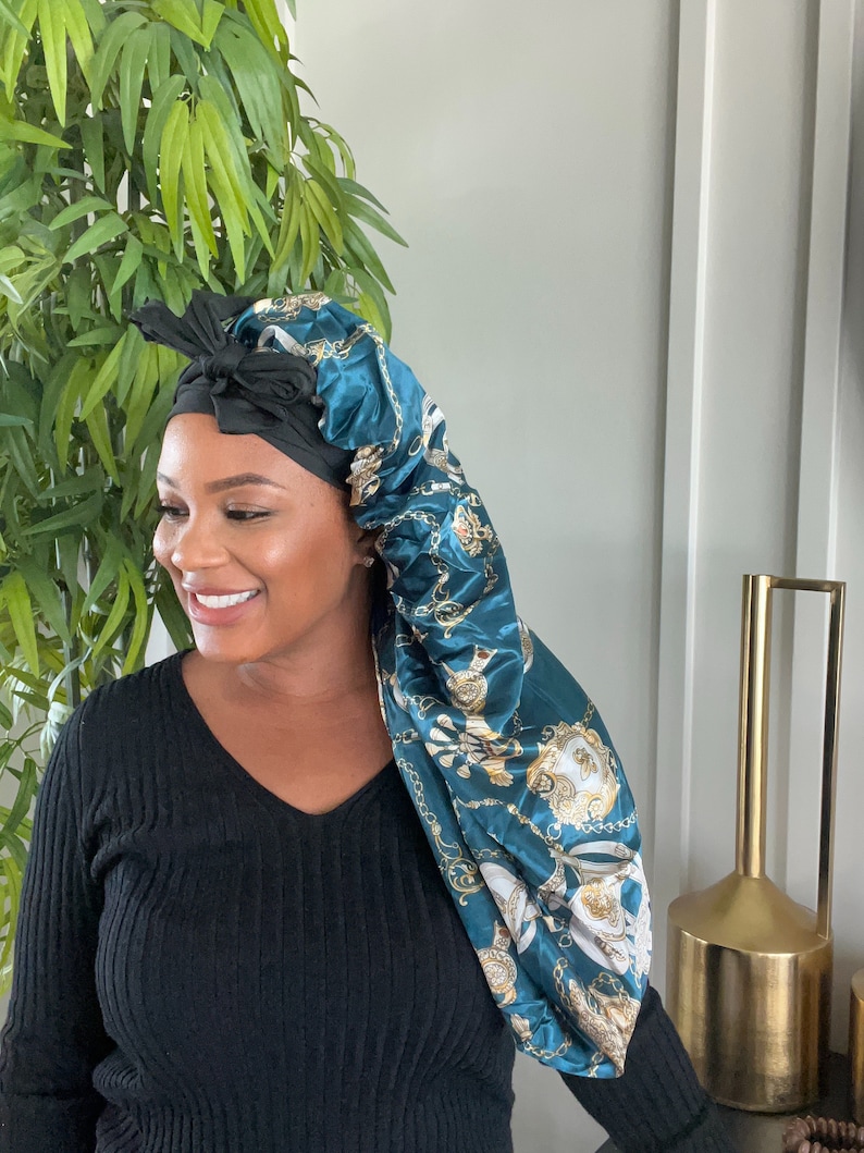 May include: A teal satin sleep cap with a gold chain print. The cap is tied with a black satin ribbon.