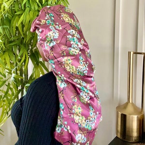 May include: A pink satin sleep cap with a floral print featuring white, yellow, and green flowers. The cap is designed to protect hair while sleeping.