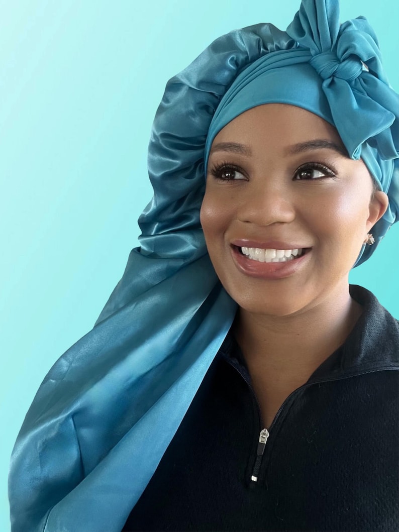 Puede incluir: Un gorro de dormir de sat&eacute;n azul turquesa con un lazo en la parte superior. El gorro lo lleva una persona de piel oscura y una gran sonrisa.