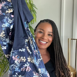 May include: A woman with long braids is holding up a blue and white floral patterned fabric. The fabric is soft and silky.