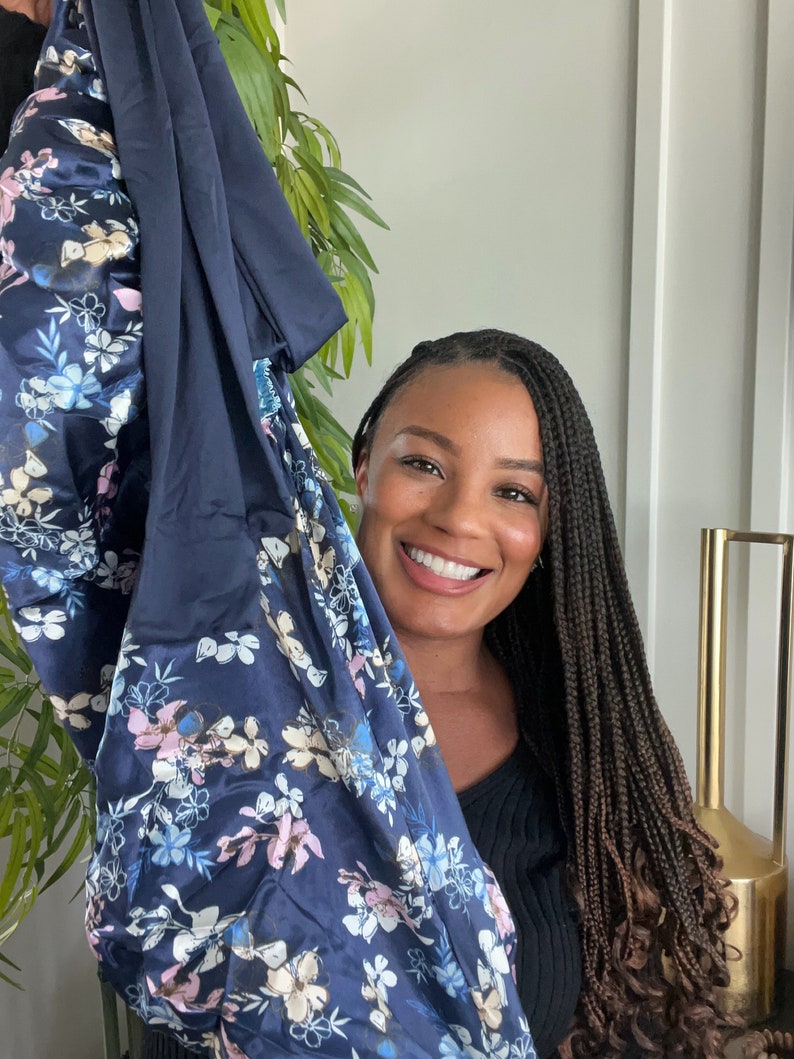 May include: A woman with long braids is holding up a blue and white floral patterned fabric. The fabric is soft and silky.