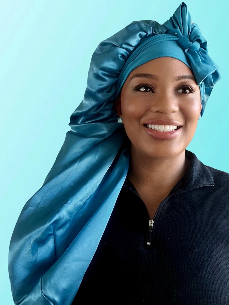 Puede incluir: Un gorro de dormir de sat&eacute;n azul turquesa con un lazo en la parte superior. El gorro est&aacute; dise&ntilde;ado para proteger el cabello mientras se duerme.