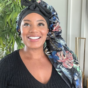 Puede incluir: Un gorro de dormir de satén negro con estampado floral. El gorro tiene un lazo en la parte superior y está diseñado para proteger el cabello mientras se duerme.