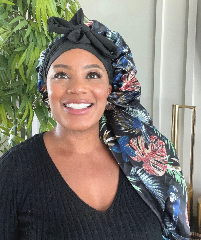 May include: A black satin sleep cap with a floral print. The cap has a bow on top and is designed to protect hair while sleeping.