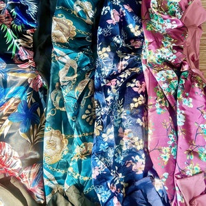 May include: Four satin hair bonnets in different patterns. The bonnets are teal with gold chains, navy blue with pink and white flowers, dark blue with white flowers, and burgundy with white flowers.