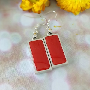 May include: A pair of silver earrings with red rectangular resin accents.