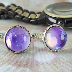 Può includere: Un paio di gemelli d'argento con cabochon di vetro iridescente viola e blu.