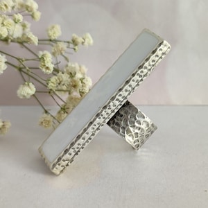 May include: A silver ring with a white rectangular stone set in a textured silver band.