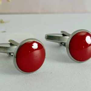 May include: A pair of silver cufflinks with red circular inlays.