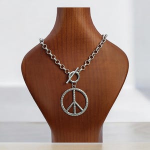 May include: A silver necklace with a peace sign pendant. The necklace has a toggle clasp and a chain link design.