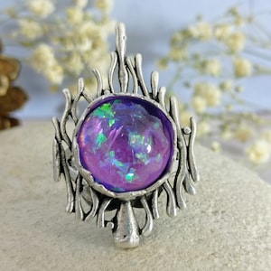 Può includere: Un anello d'argento con un cabochon iridescente viola incastonato in un design a spirale che ricorda dei rami.