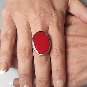 May include: A red oval ring with a gold band. The ring is on a person's finger.