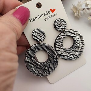 Op de afbeelding: Handgemaakte oorbellen met een zwart-zilveren zebra streepjespatroon. De oorbellen hebben een cirkelvormig ontwerp met een kleinere cirkel aan de bovenkant. De kaart leest "Handmade with love."