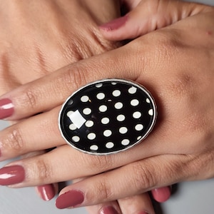 Puede incluir: Un anillo de plata con una piedra ovalada de lunares negros y blancos.