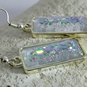 May include: A pair of silver earrings with rectangular clear resin charms filled with iridescent glitter.