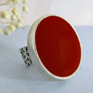 Puede incluir: Un anillo de plata con una piedra grande, redonda y roja.