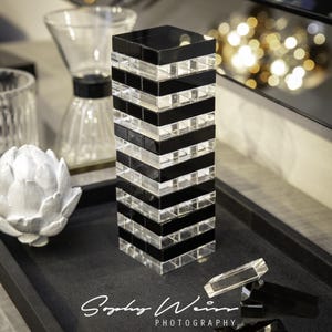 May include: A decorative tower made of alternating black and clear glass blocks. The tower is on a black tray, with additional glass pieces. The image also shows a white, artichoke-shaped sculpture and other decorative items.