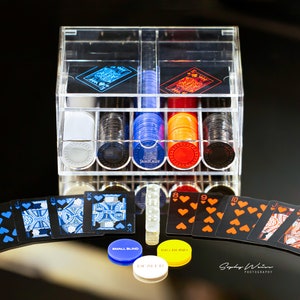 May include: A clear acrylic poker chip and card set. The set includes a clear acrylic case, poker chips in various colors, playing cards, and small blind and big blind chips. The cards are black with blue and orange suits.