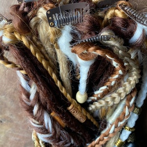 May include: A bundle of brown, blonde, and white synthetic hair extensions with clips. The extensions are braided and have wooden beads and metal rings.