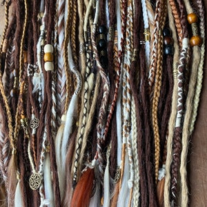 May include: A collection of brown, beige, and white synthetic dreadlocks with various beads and charms. The dreadlocks are arranged in a vertical row and are ready to be added to hair.