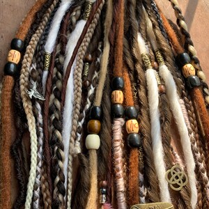May include: A set of brown, white, and black synthetic dreadlocks with wooden and metal beads. The dreadlocks are tied together with a brown leather cord.