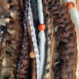 May include: Close-up of a variety of brown, black, white, and beige synthetic dreadlocks with wooden and red beads.