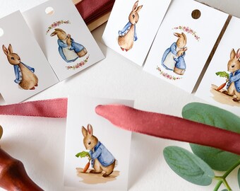 May include: Five white gift tags with watercolor illustrations of Peter Rabbit in different poses. The tags have a hole punched in the top and are tied with a red ribbon.